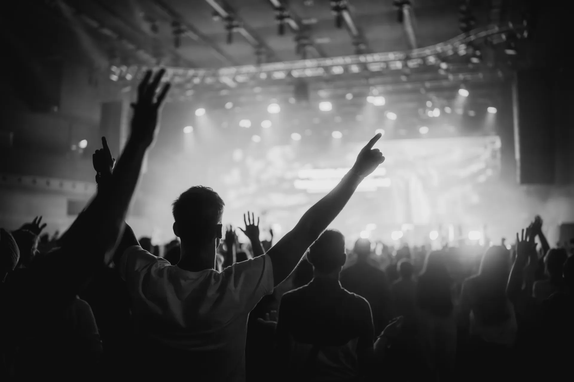 Crowd with arms raised in worship facing a brightly lit stage